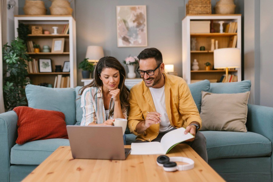 A couple sitting on a couch both looking at a computer smiling