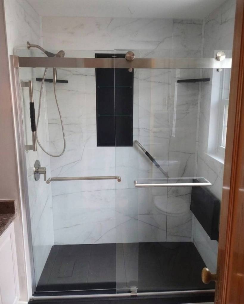 Barrier-free walk-in shower featuring sliding glass doors, built-in bench seat, strong-grip grab bars, recessed storage niche, and modern accessibility upgrades installed by The Bath Authority.