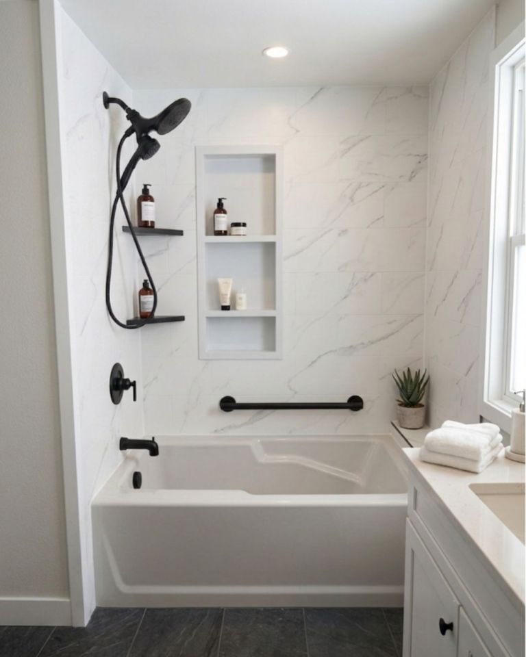 Luxury bathtub and shower remodel featuring white marble-look wall surrounds, matte black fixtures, recessed storage niche, grab bar, and built-in shelving by The Bath Authority.