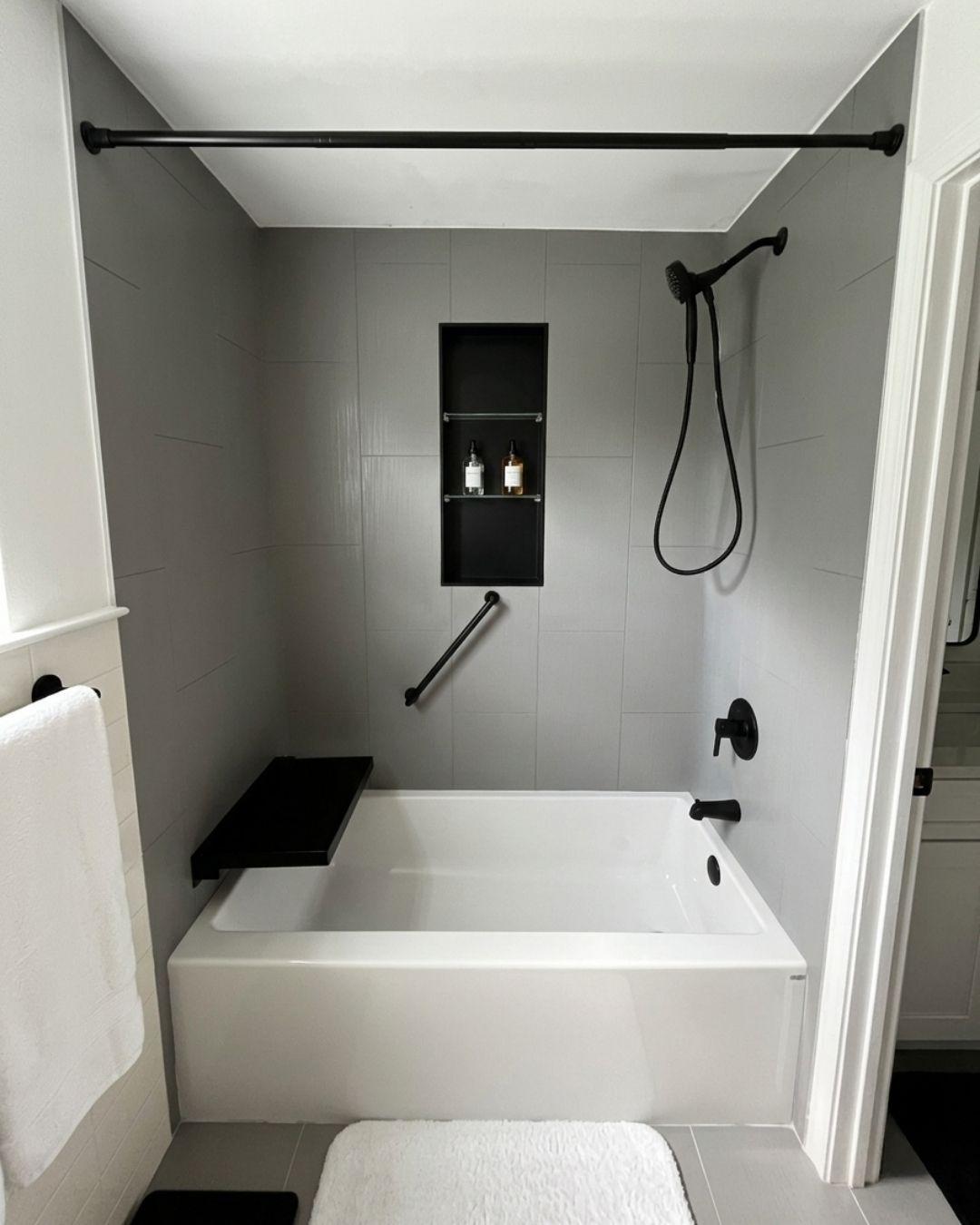 Modern bathtub replacement with gray wall surrounds, matte black shower fixtures, built-in bench seat, recessed storage niche, and grab bar installed by The Bath Authority.