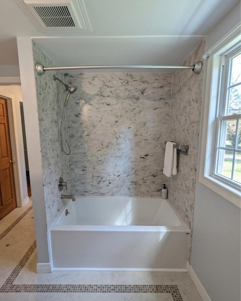Elegant soaking tub with gray-and-white marble-pattern wall surrounds, brushed nickel fixtures, and spacious alcove design remodeled by The Bath Authority.