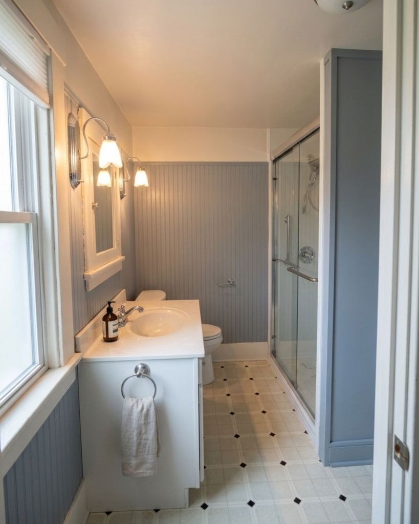 Compact full bathroom renovation completed by The Bath Authority with gray beadboard walls, updated vanity, glass shower enclosure, new flooring, and space-saving bathroom design.