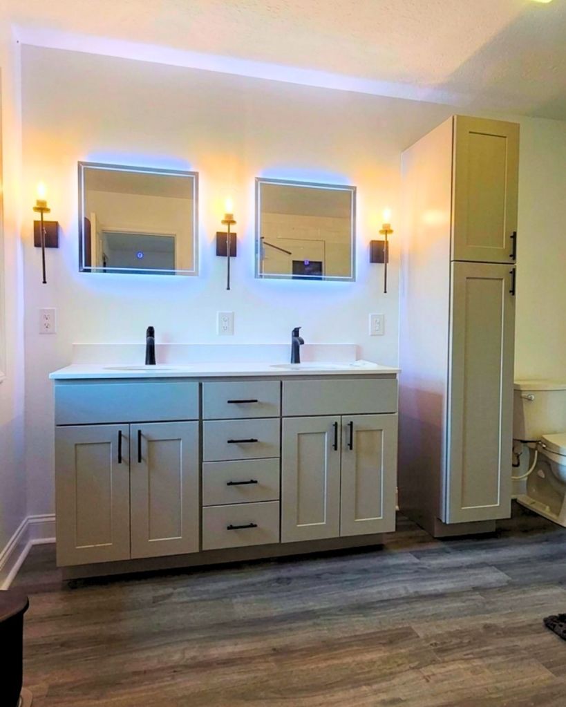Double-sink bathroom vanity installation completed by The Bath Authority with shaker cabinetry, quartz countertop, black fixtures, modern sconces, and built-in storage tower.