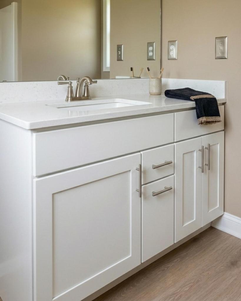 Custom bathroom vanity remodel completed by The Bath Authority featuring white shaker cabinets, quartz countertop, brushed nickel fixtures, and a large wall mirror for a clean modern look.