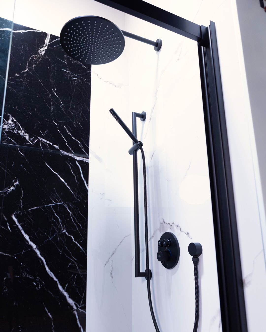 Modern walk-in shower with matte black rainfall showerhead, handheld sprayer, marble-look wall panels, and glass enclosure by The Bath Authority.