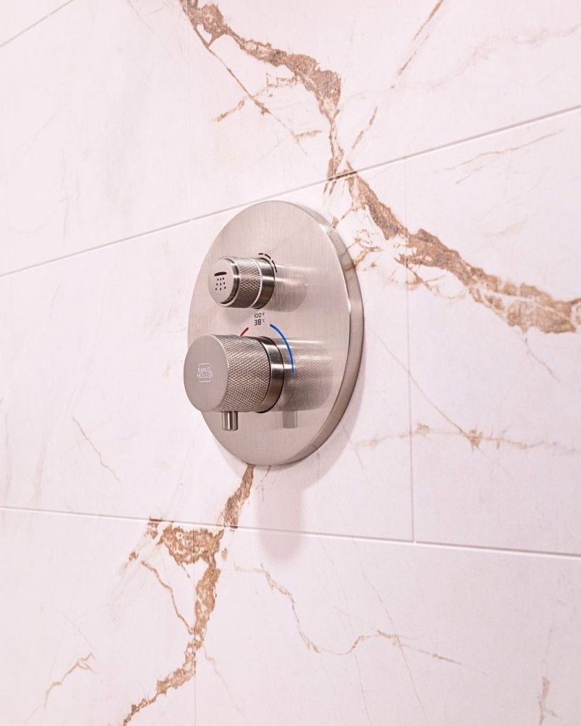 Close-up of brushed nickel thermostatic shower valve mounted on white marble-look wall panels installed by The Bath Authority.