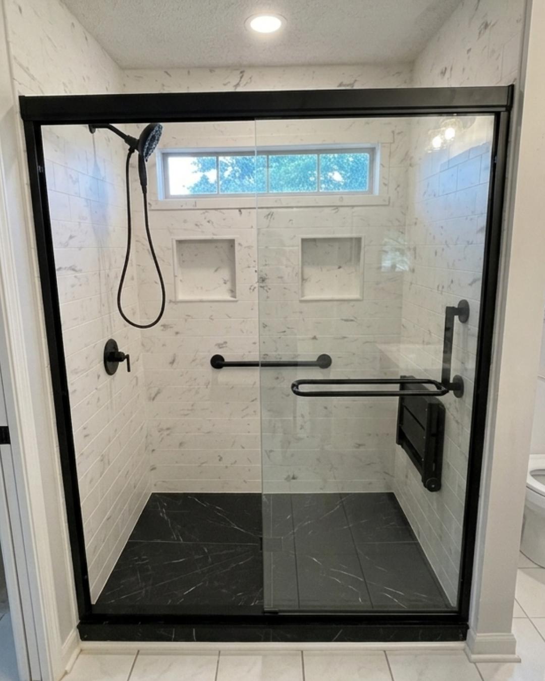 Walk-in shower with black-framed glass doors, marble tile-look walls, built-in niches, grab bars, and dark shower base by The Bath Authority.