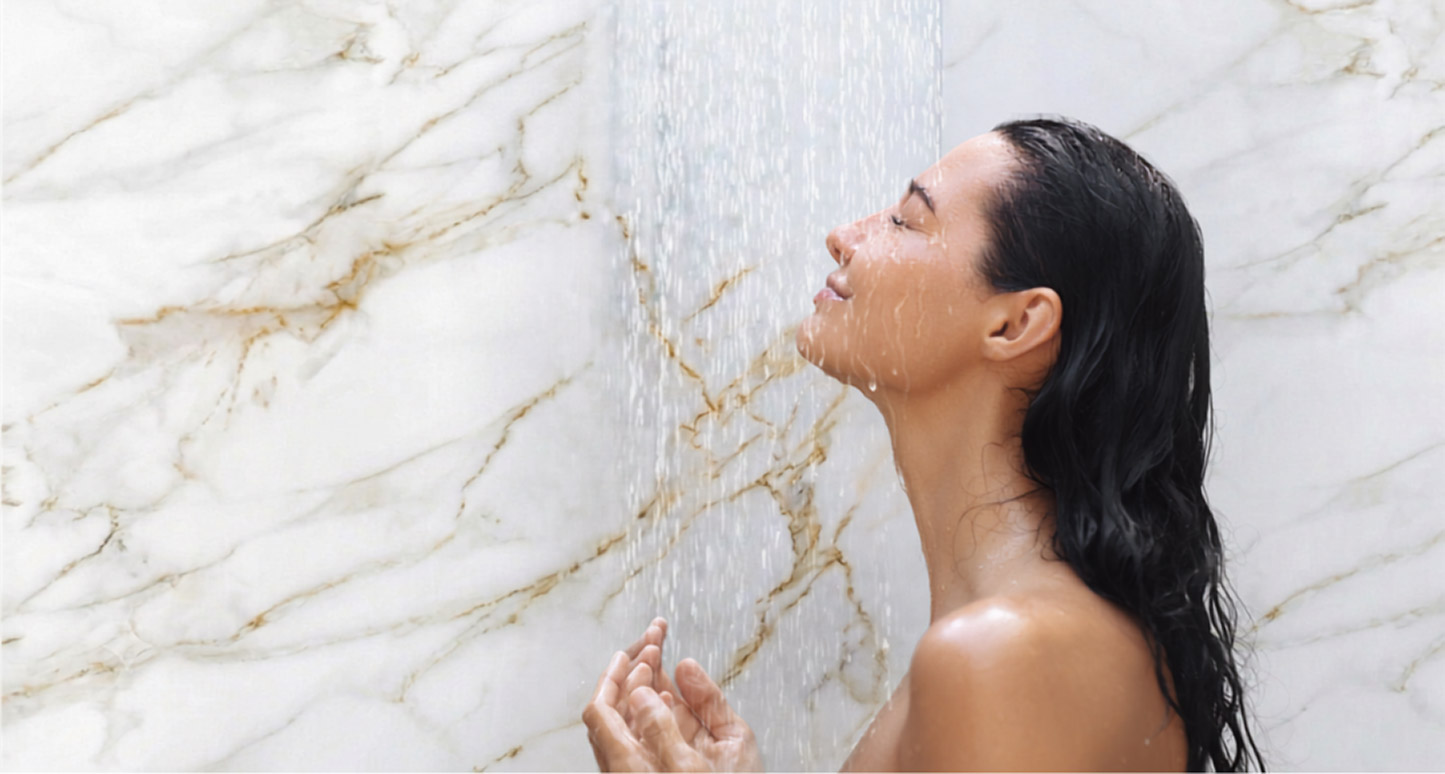A woman stands in a shower smiling while the water drips down her face.