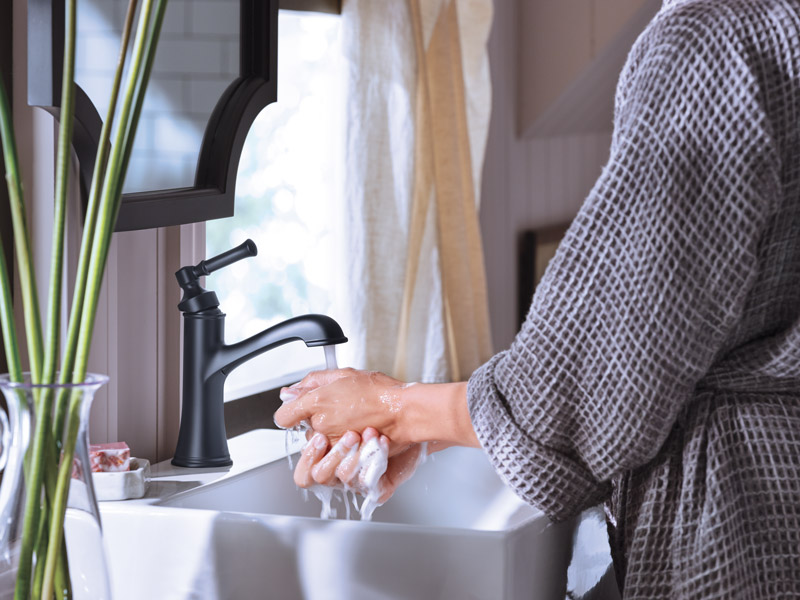A woman in a bathrobe stands at a bathroom sink washing her hands.