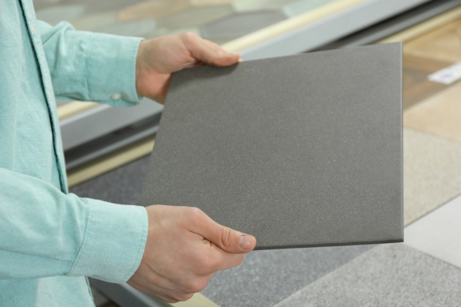 A man holds a large tile sample of a dark gray concrete color.