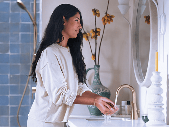 A woman smiles as she looks in the bathroom mirror while washing her hands.