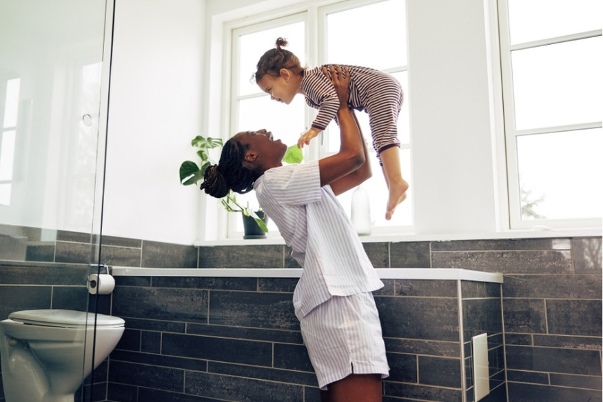 A woman playfully lifts her daughter in the air in their bathroom at home.