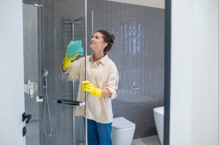 Woman stands in shower at home to clean the shower wall.