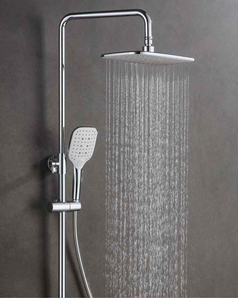 The water runs out of a chrome rainfall showerhead in front of a dark concrete shower surround.
