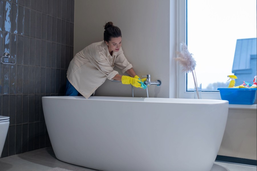 Woman cleaning her bathtub wearing gloves